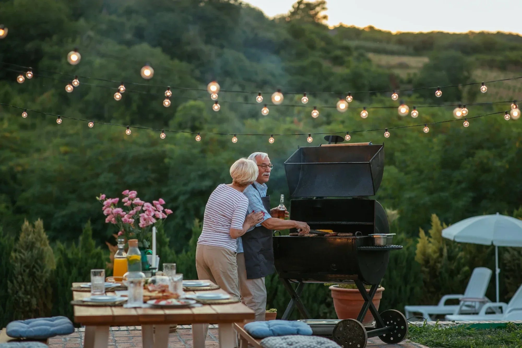 Glückliches Seniorenpaar tanzt unter warmen Lichterketten im Garten am Abend