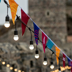 Bunte Wimpelketten mit warmweißen Außenlichtern im Garten bei einer Outdoor-Party
