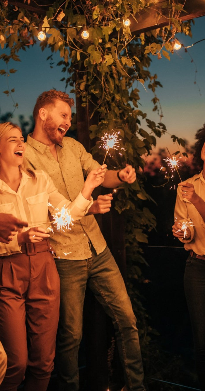 Freunde feiern im Garten mit Lichterketten und Wunderkerzen