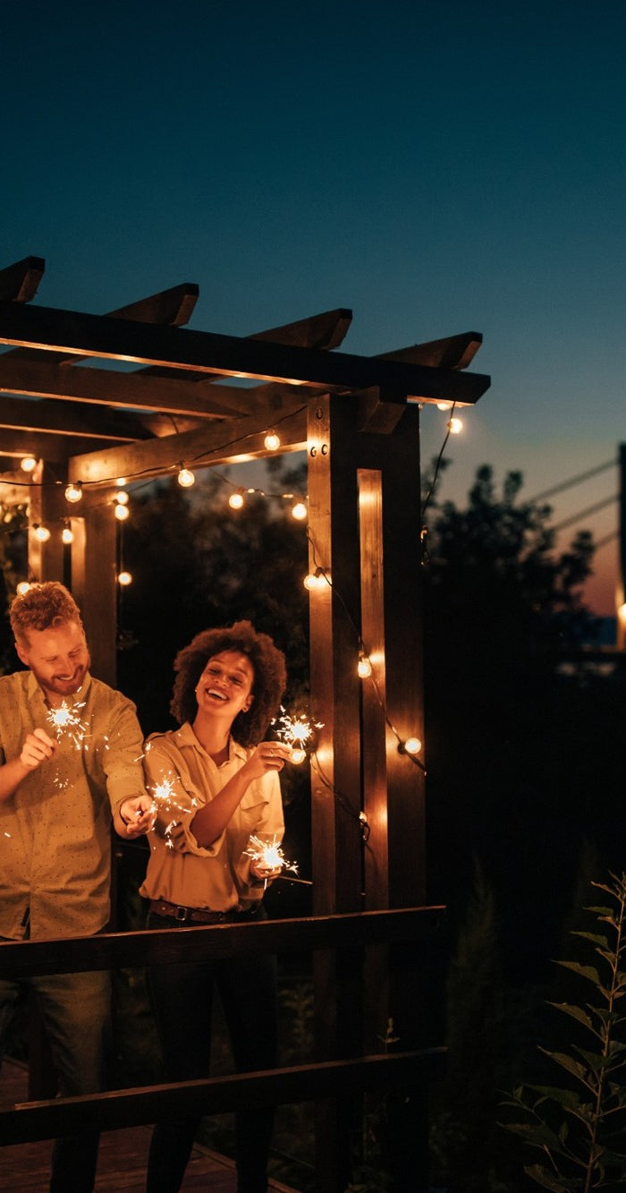 Freunde feiern eine Gartenparty am Abend mit Lichterketten und Wunderkerzen